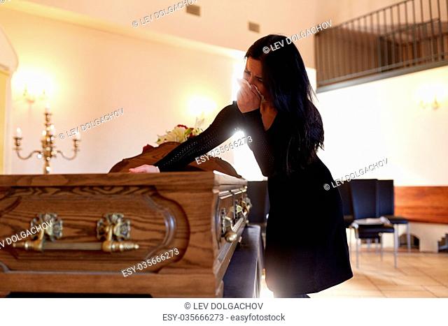 people and mourning concept - crying woman with coffin at funeral in church