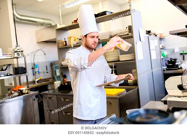 cooking, profession and people concept - male chef cook with clipboard doing inventory in restaurant kitchen