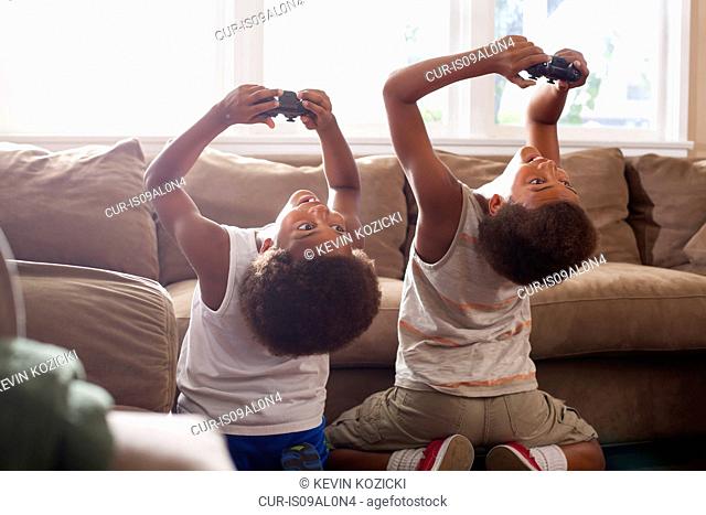 Two brothers bending backwards whilst playing game controllers in living room