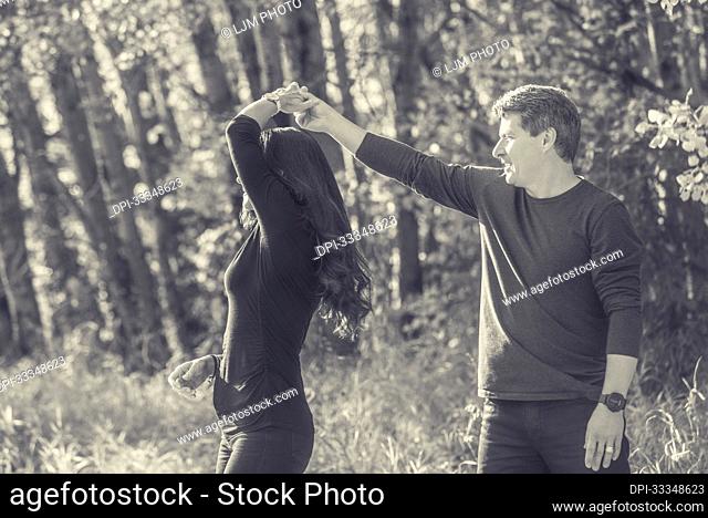 Mature couple dancing in the autumn leaves and enjoying each other's company while taking a walk in the woods; St Albert, Alberta, Canada