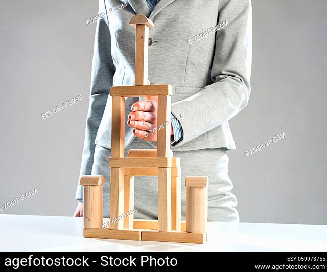 Business woman building tower on table from wooden blocks. Strategy planning and development concept. Young woman wearing formal wear sitting in office interior