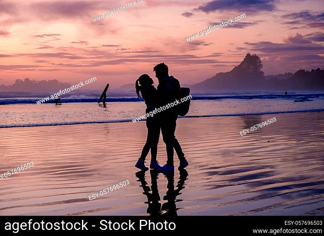 couple of men and women mid-age watching the sunset on the beach of Tofino Vancouver Island Canada, beautiful sunset on the beach with pink-purple colors in the...