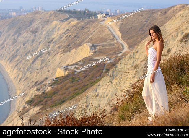 A girl stands on a mountainside at sunset against a beautiful landscape