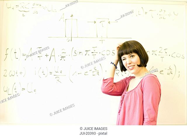 Portrait of confused young woman standing before an equation on the board