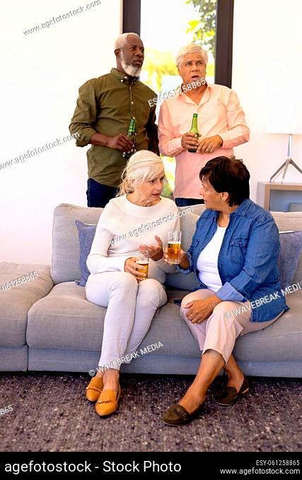 Multiracial senior females with beer talking while men watching match seriously in nursing home
