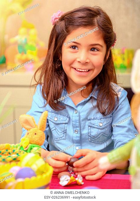 Portrait of nice little girl opening small chocolate egg, having fun at home, preparing to happy religious spring holiday, Easter
