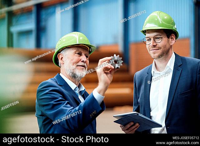 Male professional discussing over equipment with coworker in factory