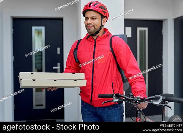 Deliveryman with pizza boxes and bicycle standing in front of house door