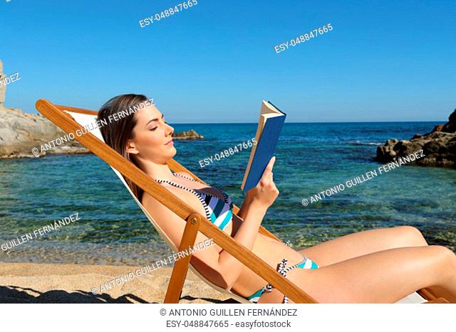 Side view portrait of a tourist reading a book on a hammock on the beach on summer vacation