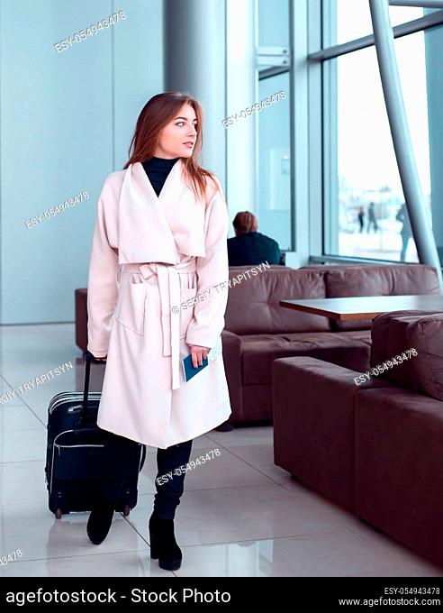 Young female traveller walking the airport hall draging suitcase