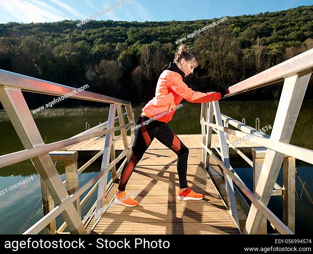 Young athlete woman exercises and stretches on the platform of a river