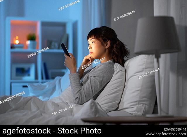 asian woman with smartphone in bed at night