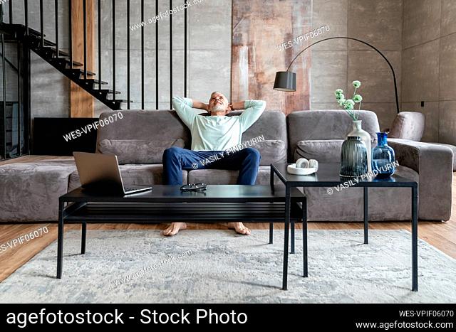 Man with hands behind head resting on sofa at home