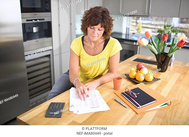 Woman sitting in kitchen doing paperwork