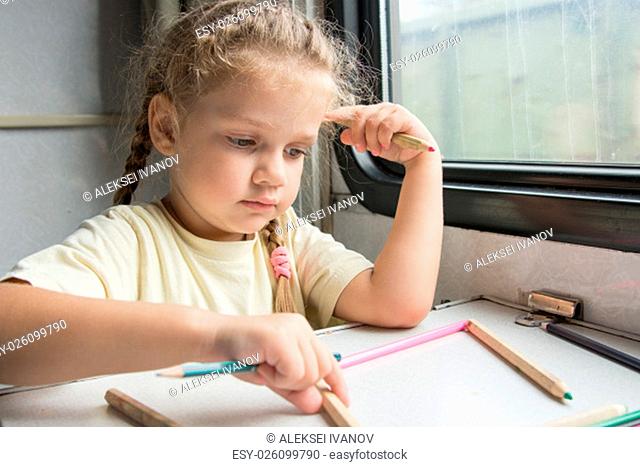 Four-year girl draws pencil in a notebook for a side table in the second-class train carriage