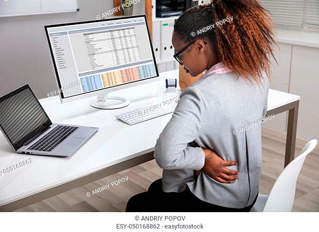 Side View Of African Businesswoman Holding Her Back While Working On Laptop At Office Desk