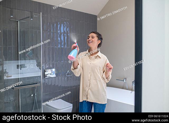 Air freshening. A smiling young woman spraying the air freshener in the bathroom