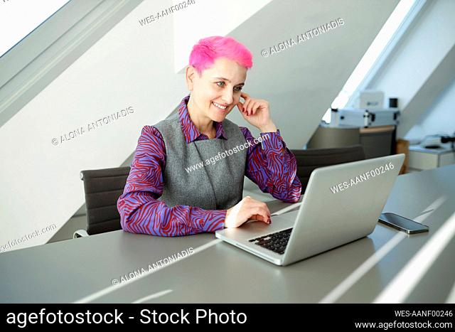 Smiling businesswoman with pink hair working on laptop at office