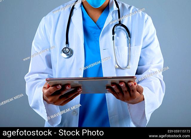 Mid section of female doctor holding digital tablet against grey background