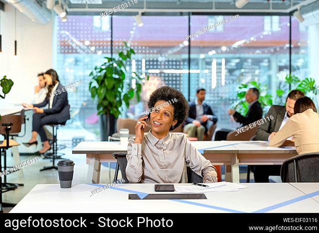 Businesswoman talking on smart phone and colleagues working in background at office