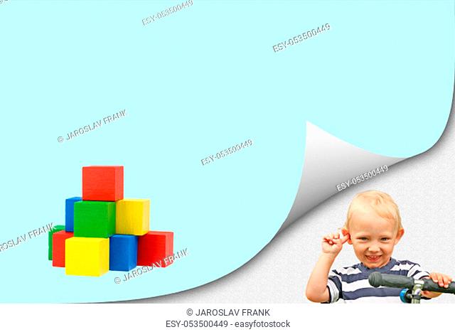 Child play with wooden toys concept. Smiling blond boy is standing in an exposed corner next to a blank blue page with a 3d pyramid created from colorful wooden...