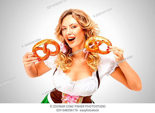 Beautiful Oktoberfest woman wearing a traditional Bavarian dress dirndl holding pretzels, on grey background