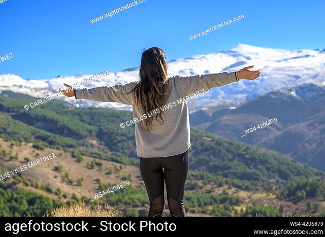 Hiker on her back with arms outstretched happily enjoying the scenery while walking outdoors in winter,
