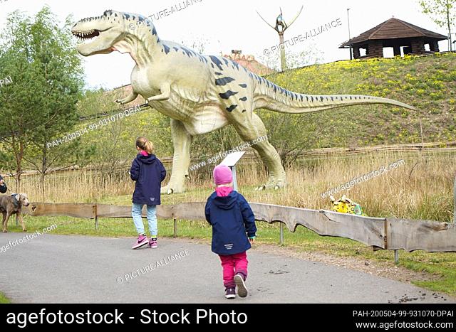 01 May 2020, Berlin: Children walk past a life-size model of a Tyrannosaurus dinosaur in the Germendorf Animal, Leisure and Prehistoric Park