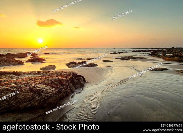 Beach in golden sunset light during low tide showing stream of water and rocks covered with sea algae. Kantiang Bay, Ko Lanta, Thailand