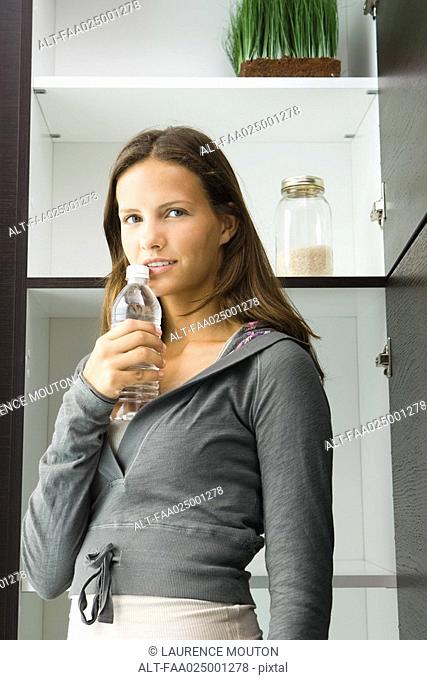 Teen girl standing by pantry, holding bottle of water