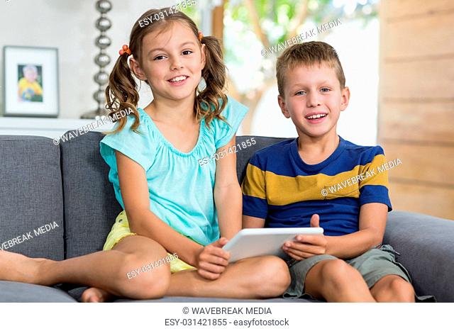 Portrait of siblings with digital tablet sitting on sofa in living room