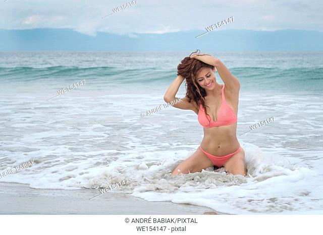 Hispanic woman in bikini smiling happily while sitting in the water