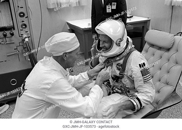 Astronaut L. Gordon Cooper Jr., Gemini-5 command pilot, gets help with the donning of his spacesuit by NASA suit technician Clyde Teague during suiting up...
