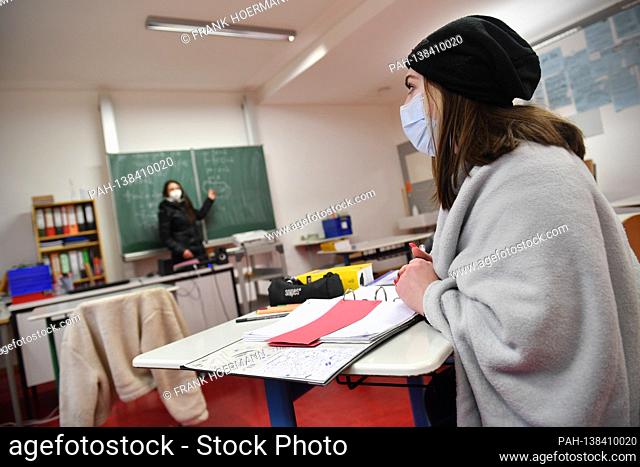 School lessons in times of the coronavirus pandemic. Teacher stands at a blackboard, school blackboard - a student sits on her seat and listens to the lesson