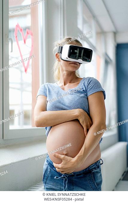 Pregnant woman wearing VR glasses at the window