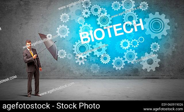 Businessman defending with umbrella from BIOTECH inscription, technology concept