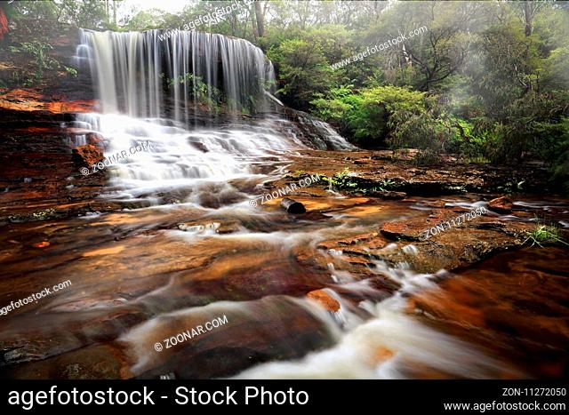 Weeping rock, a tranquil lush waterfall, seen here spilling over and flowing downstream. Blue Mountains Australia