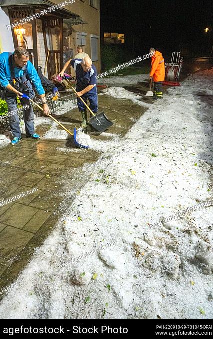 09 September 2022, Mecklenburg-Western Pomerania, Stralsund: Men shovel hailstones from the sidewalk with snow pushers. Cellars and apartments were flooded by...