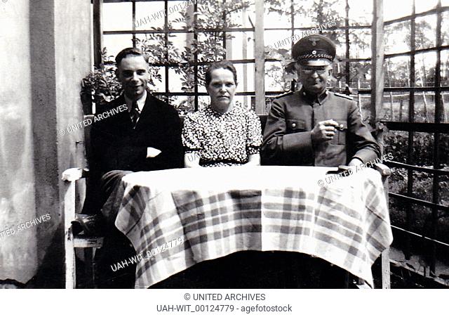 Ein junges Paar sitzt mit einem älteren Uniformierten am Gartentisch., Sammlung Wittmann