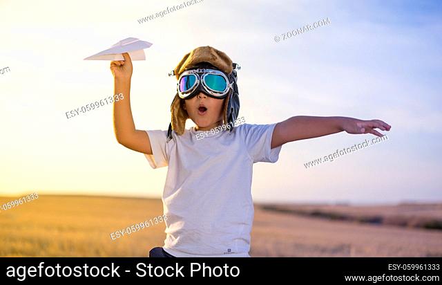 Little boy wearing helmet and dreams of becoming an aviator while playing a paper plane at sunset
