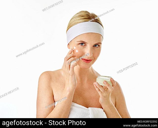 Woman applying face cream while standing against white background