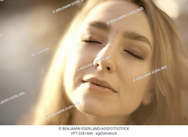 headshot of young woman outdoors with closed eyes enjoying sunlight, in Cottbus, Brandenburg, Germany