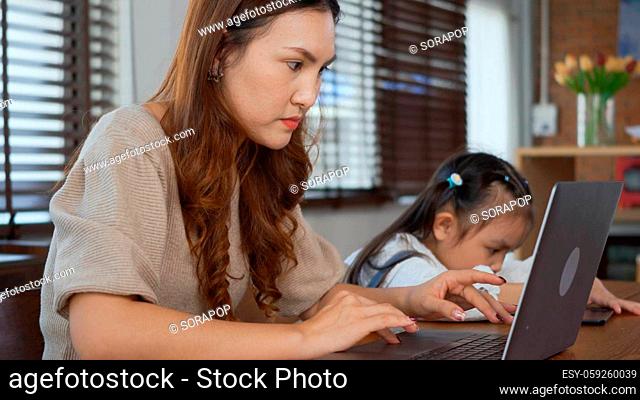 Asian young mother working with laptop computer at home and help daughter doing homework, Single mom freelancer work from home and helping his girl kid teaching...