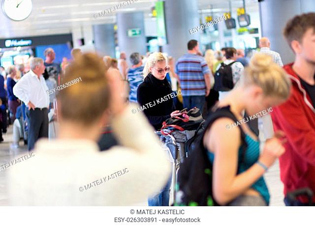 Casual blond young woman using her cell phone while queuing for flight check-in and baggage drop. Wireless network hotspot enabling people to access internet...