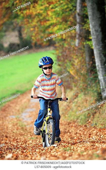 boy riding his bicycle on road with leaves in fall, autumn foliage covering path in forest, autumn, fall, Zuerich, Switzerland