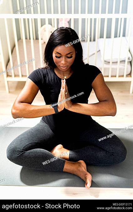 Pregnant woman with hands clasped doing yoga in front of crib