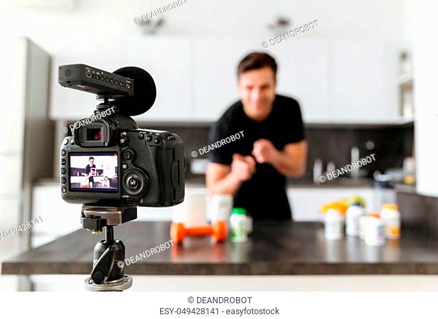Happy young man filming his video blog episode about healthy food additives while standing at the kitchen table and pointing finger at camera