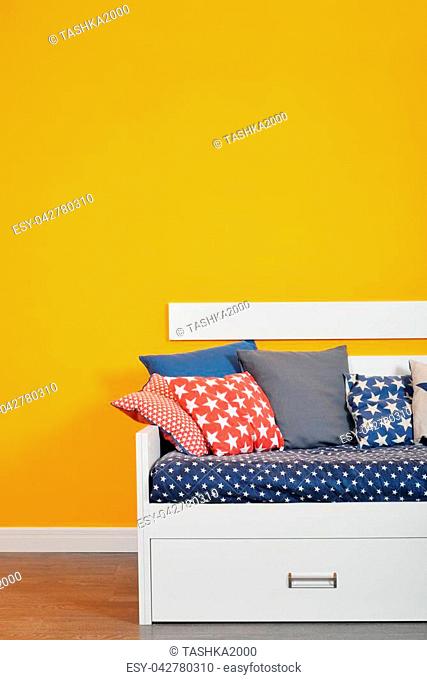 Children's bed bed with different color pillows against orange wall in the room