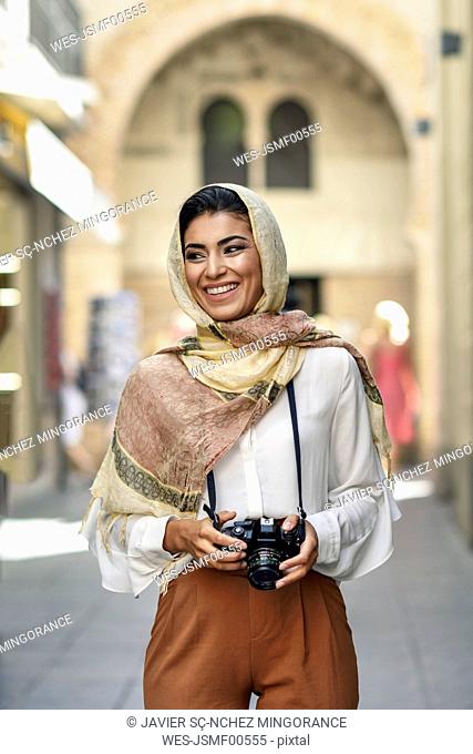 Spain, Granada, young Arab tourist woman wearing hijab, using camera during sightseeing in the city
