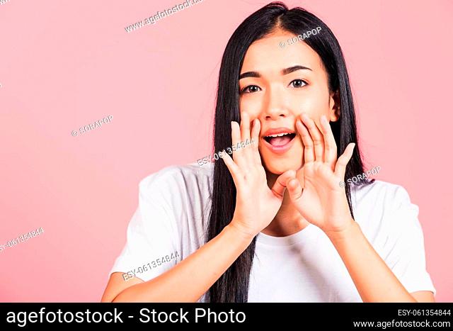 Asian happy portrait beautiful cute young woman teen standing hand on mouth talking whisper secret rumor studio shot isolated on pink background
